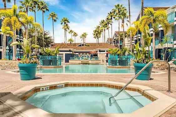 Bilde av et basseng omgitt av solsenger og palmer. I forgrunnen er det et mindre boblebad med gelender. (AI-generert tekst)