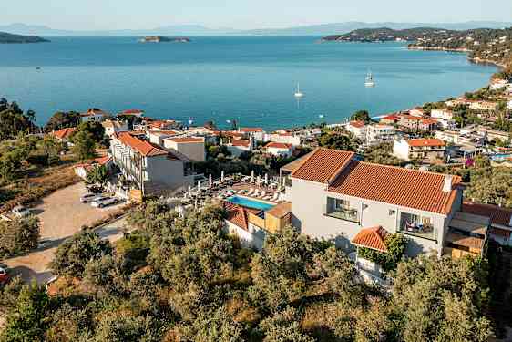 En utsikt over en kystby med røde tak på hvite bygninger, omgitt av grøntområder og med blått hav i bakgrunnen. (AI-generert tekst)