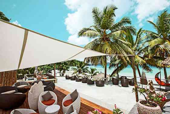 Utendørsområde med sitteplasser og palmetrær ved en strand. (AI-generert tekst)