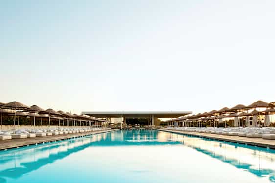 Et stort og langt basseng med parasoller og solsenger på begge sider. (AI-generert tekst)