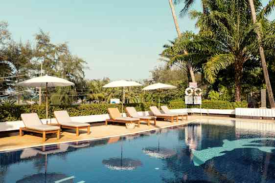 Et utendørsbasseng med solsenger og parasoller. Tropiske trær i bakgrunnen. (AI-generert tekst)