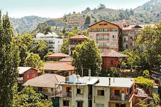 En samling bolighus blant trær ved en skråning. (AI-generert tekst)