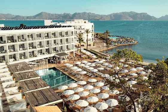 Hotellkompleks ved vannkanten med solsenger og parasoller rundt et basseng. (AI-generert tekst)