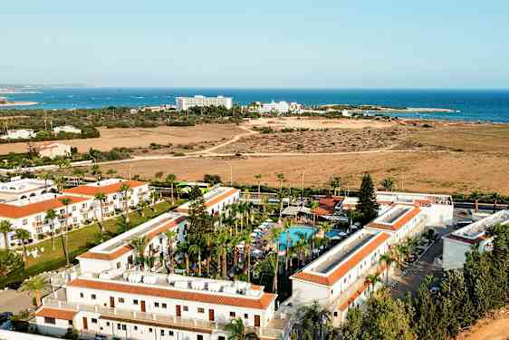 Luftfoto av et hotellområde med basseng og havet i bakgrunnen. (AI-generert tekst)