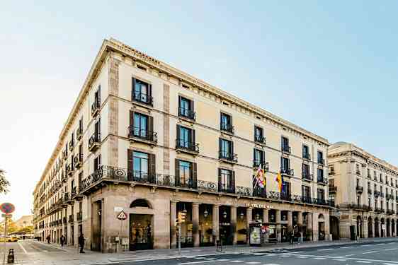 Et gatehjørne med en bygning i klassisk stil, med flere etasjer, buer og dekorerte balkonger. (AI-generert tekst)