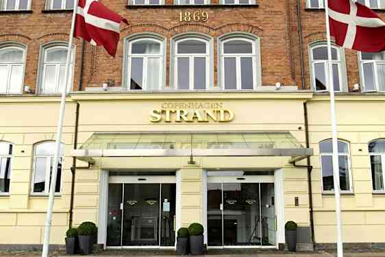Hotellfasade med skilt som sier 'Copenhagen Strand'. Danske flagg sees ved inngangen. (AI-generert tekst)