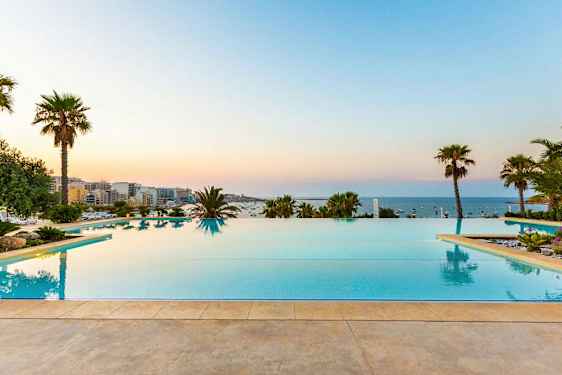 Infinity-basseng med utsikt over havet, omgitt av palmer og grøntområder. (AI-generert tekst)