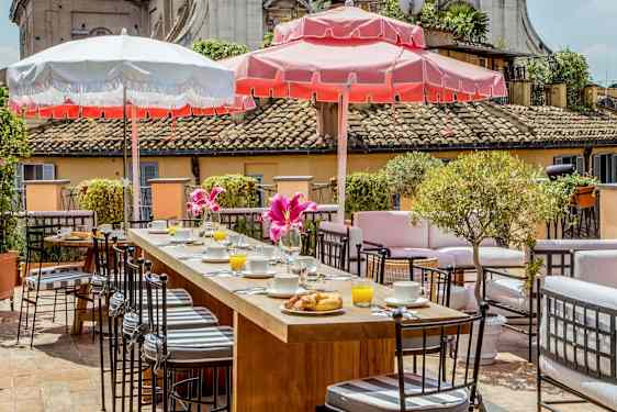 En terrasse med sittegrupper, frokostservering og parasoller i solfylt vær. (AI-generert tekst)