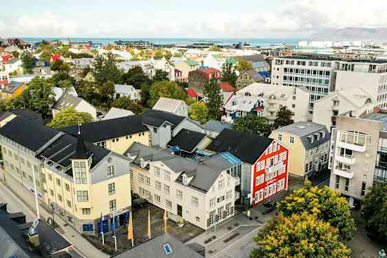 En byutsikt med fargerike bygninger, trær og en vei, samt bakgrunn med hav og fjell. (AI-generert tekst)