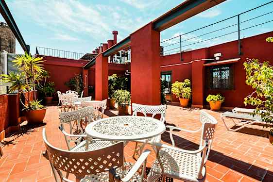 En terrasse med hvite metallmøbler og potteplanter på et teglgulv, omgitt av rødmalt vegger. (AI-generert tekst)