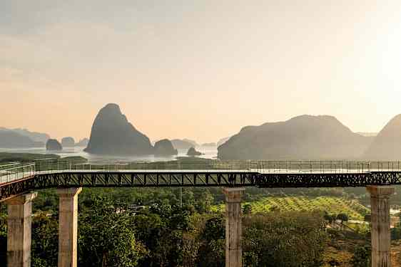 En bro med søyler leder til et område med vann og fjell i bakgrunnen. (AI-generert tekst)