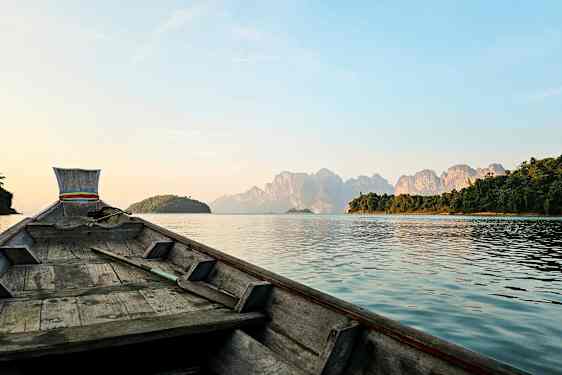 Bilde av en trebåt som seiler mot fjell på en innsjø. (AI-generert tekst)