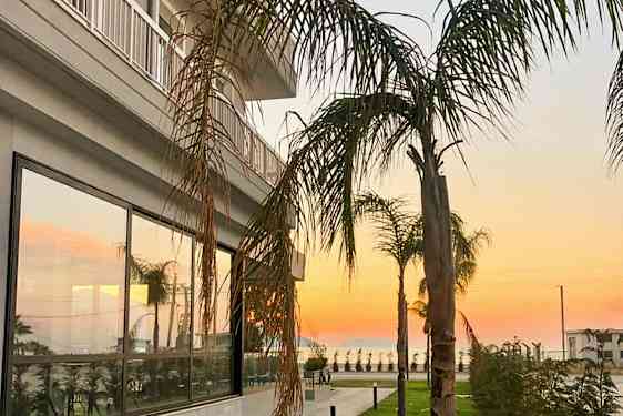 En bygning med glassvinduer og palmer i forgrunnen ved solnedgang. (AI-generert tekst)