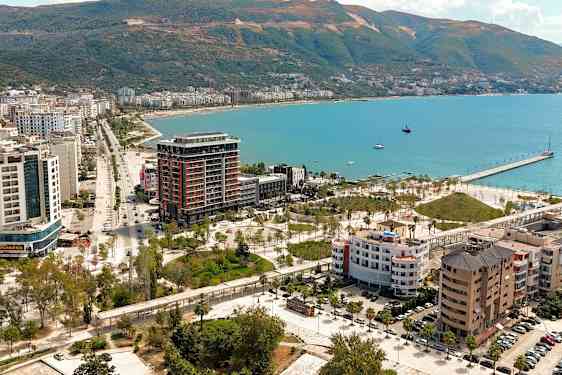 Utsikt over en kystby med bygninger, grøntområder og en brygge ved havet. (AI-generert tekst)