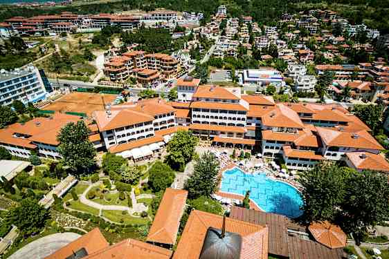 Flyfoto av et feriested med røde hustak, et basseng og omkringliggende grøntområder. (AI-generert tekst)