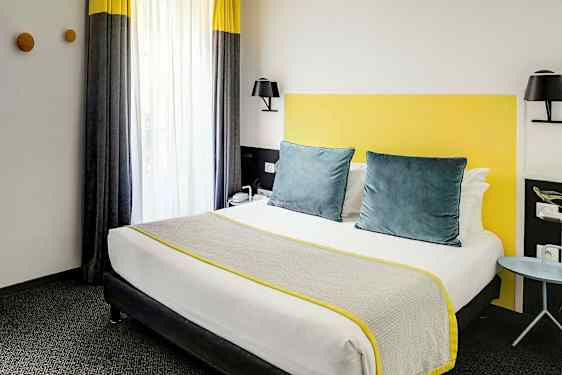 Et hotellrom med en seng utstyrt med grå og gule detaljer. (AI-generert tekst)