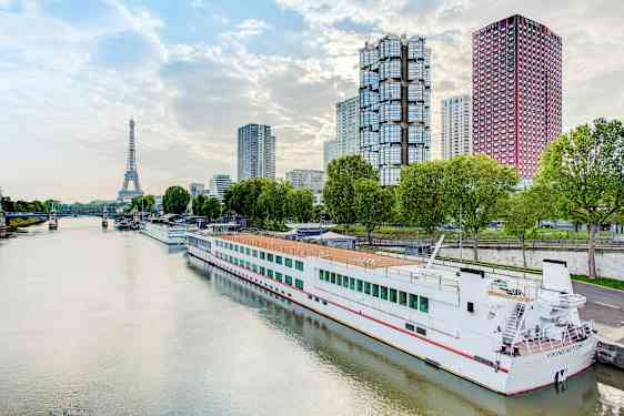 Elv med en båt ved kai, moderne bygninger og Eiffeltårnet i bakgrunnen. (AI-generert tekst)