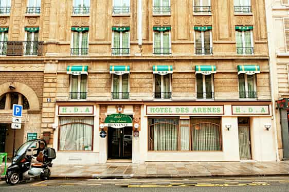 Bygning med hotellfasade, skilt med teksten 'Hotel des Arenes' og grønnhvite markiser over vinduene. (AI-generert tekst)