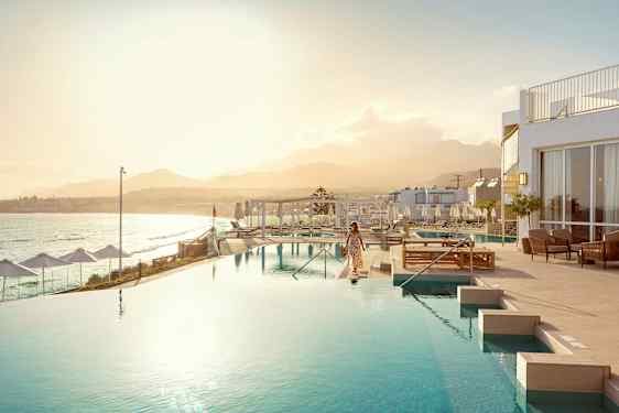 En kvinne ved et infinitybasseng med havet og en fjellkjede i bakgrunnen. (AI-generert tekst)