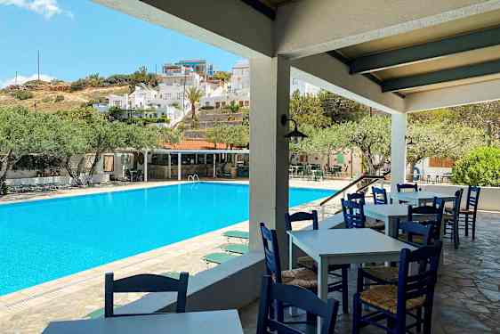 Utendørsbasseng med stoler og bord i forgrunnen og bygninger i bakgrunnen. (AI-generert tekst)