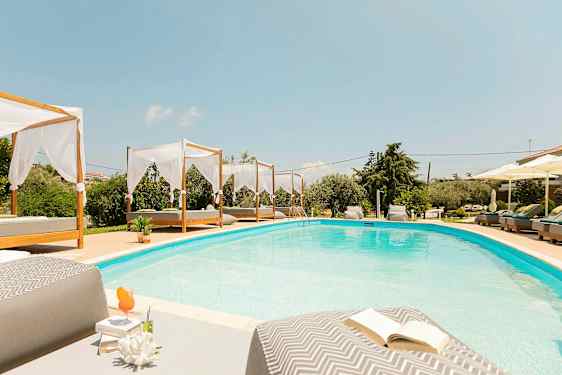 Et svømmebasseng med senger og parasoller rundt. (AI-generert tekst)