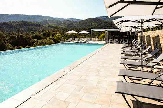 Et evighetsbasseng med solsenger og parasoller ved siden av, plassert med utsikt over et naturskjønt fjellandskap. (AI-generert tekst)