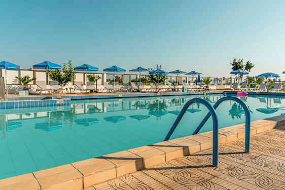 Et bilde av et utendørs basseng med blå parasoller og solsenger rundt. (AI-generert tekst)