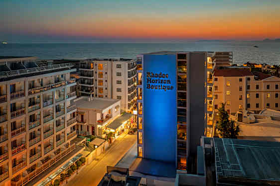 Utsikt over et hotellområde med havet i bakgrunnen ved solnedgang. (AI-generert tekst)