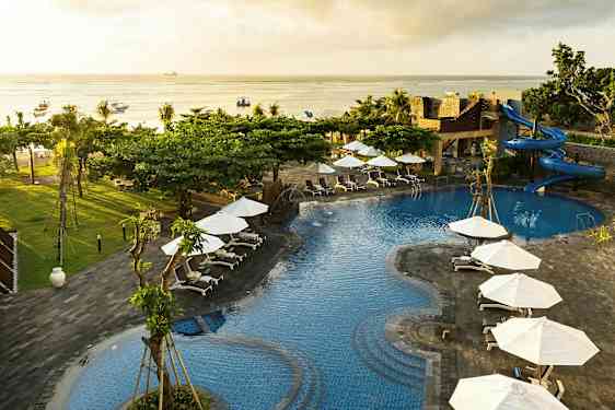 Bildet viser et bassengområde med blått vann, omgitt av solsenger og hvite parasoller. Det finnes en vannsklie og utsikt mot havet. (AI-generert tekst)