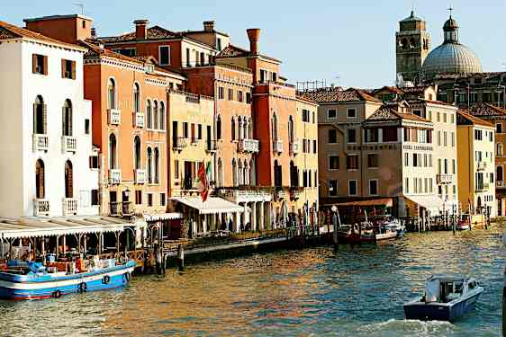 Et bilde av en kanal i Venezia med fargerike bygninger, båter og en kuppelformet kirke i bakgrunnen. (AI-generert tekst)