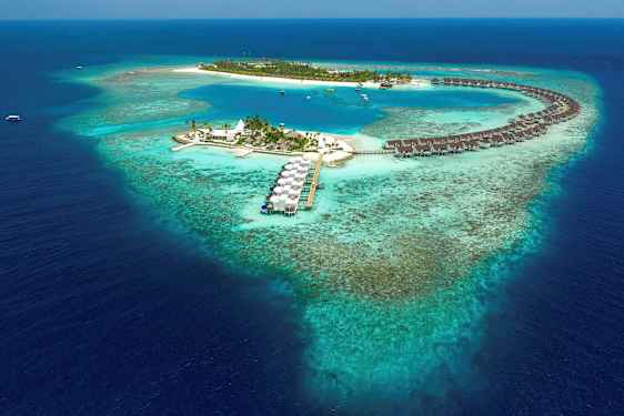 Flyfoto av en tropisk øy med overvannsbungalower og blå lagune omgitt av korallrev. (AI-generert tekst)