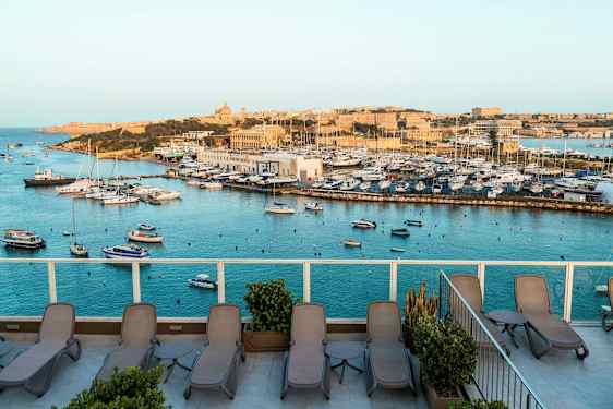 Utsikt over en marina med båter og en terrasse med solsenger. (AI-generert tekst)