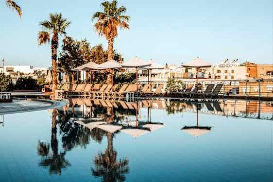 Et basseng med parasoller og solsenger på en solrik dag. (AI-generert tekst)