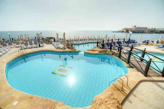 Bilde av et utendørsbasseng ved stranden med solsenger og parasoller rundt. (AI-generert tekst)