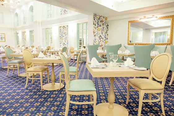 Et lyst og elegant innredet spisestue med dekkede bord og stoler, omgitt av vegger med mønstrede tapeter. (AI-generert tekst)