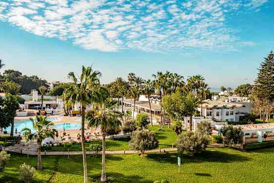 Hotellområde med gressplener, palmer, basseng og hvite bygninger. (AI-generert tekst)