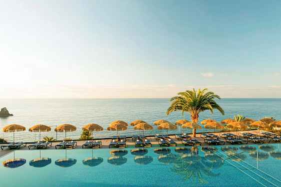 Et evighetsbasseng med solsenger og parasoller ved sjøen. (AI-generert tekst)