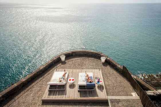 En terrasse med to solsenger og havet i bakgrunnen. (AI-generert tekst)