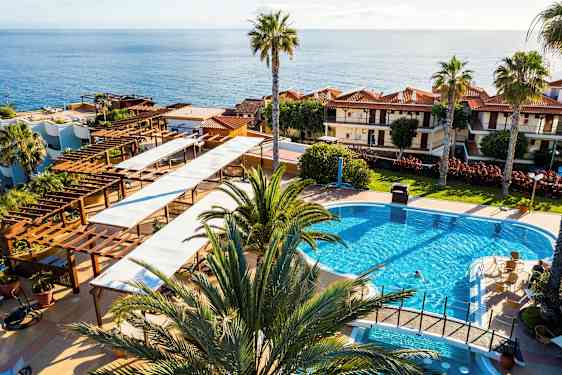 Utsikt over et hotellområde med basseng, palmer og sjø i bakgrunnen. (AI-generert tekst)