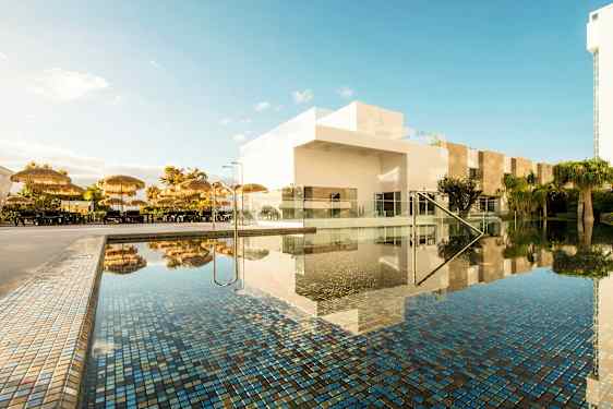 Bassengområde med parasoller og hvite bygninger. (AI-generert tekst)