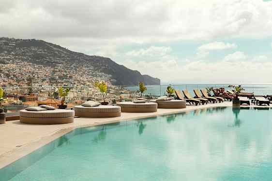 Et infinitybasseng med solsenger og utsikt over en by og fjell. (AI-generert tekst)