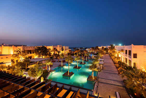 Et opplyst feriested med bassenger og palmer på kveldstid. (AI-generert tekst)