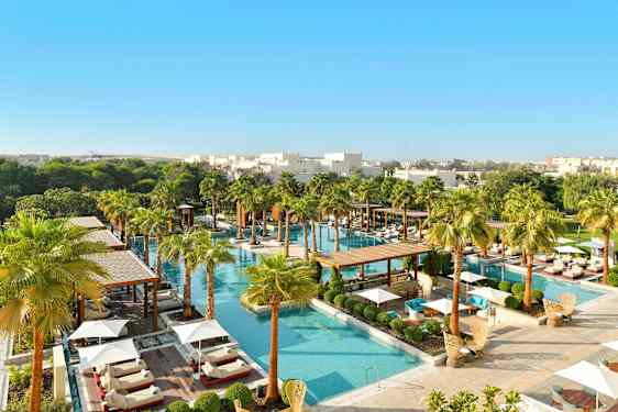 Et luksuriøst bassengområde omgitt av grøntområder og palmer, med solsenger og parasoller. (AI-generert tekst)