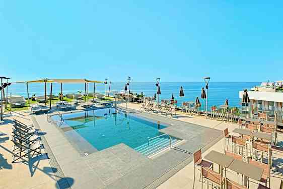 Utendørsbasseng med solsenger og parasoller, samt havutsikt. (AI-generert tekst)