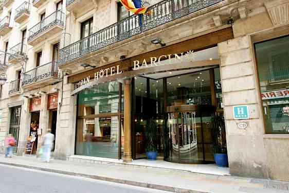 Et hotell med en glassinngang og dekorativt skilt over, plassert ved en gate med fortau. (AI-generert tekst)