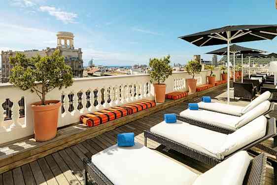 Utsikt over en terrasse med solsenger og parasoller, med en by og havet i bakgrunnen. (AI-generert tekst)