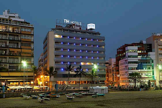 Bilde av et hotell ved sjøen om kvelden, med lysskilt og omgivelser. (AI-generert tekst)