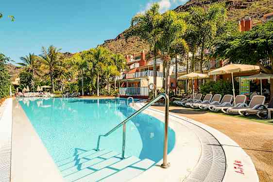 Utendørsbasseng med solsenger ved et hotell, omgitt av palmer og grønne planter. (AI-generert tekst)