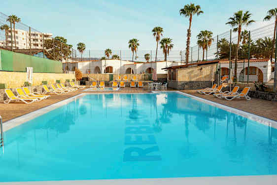 Svømmebasseng utendørs med solsenger og palmer i bakgrunnen. (AI-generert tekst)