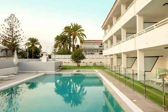 Utendørs svømmebasseng med gjerde og omkringliggende bygninger i bakgrunnen. (AI-generert tekst)